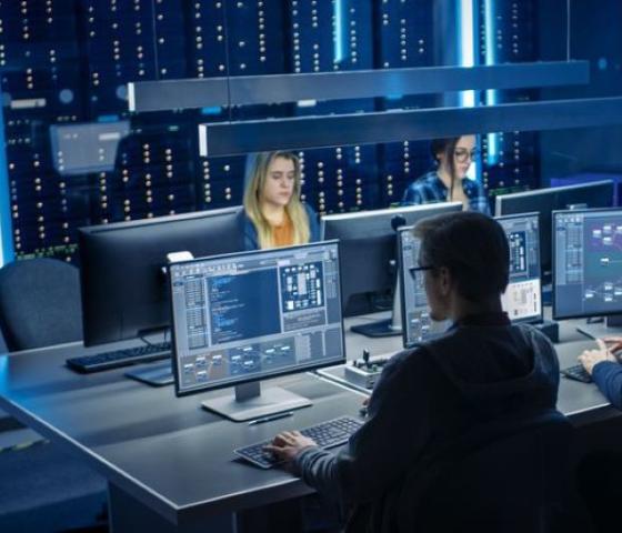 Three young people working with laptops and computer monitors